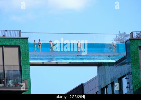 London, Großbritannien. Schwimmer am neu eröffneten Sky Pool in Embassy Gardens winken zur Kamera. Der transparente Pool ist zwischen zwei Gebäuden aufgehängt. Stockfoto