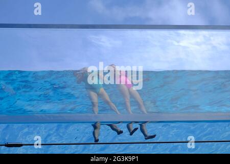 London, Großbritannien. Zwei Schwimmer am Embassy Gardens Sky Pool kommen an den Rand der transparenten Acrylstruktur, die sich in einer Höhe von 1,2 m in der Luft befindet. Stockfoto