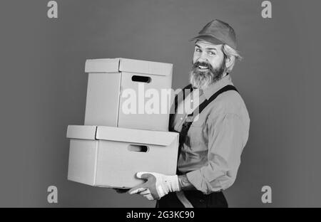 Mann trägt boilersuit Verpackung Boxen. Umzug in eine neue Wohnung. Bärtige Lader in Uniform. Pappkartons - Umzug in ein neues Haus. Kauf von neuen Stockfoto