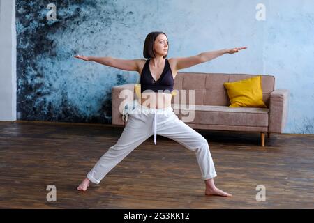 Frau in ihrem Wohnzimmer in Krieger-Yoga-Pose. Stockfoto