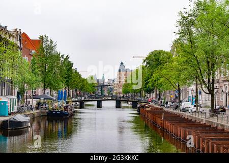 AMSTERDAM, NIEDERLANDE. 06. JUNI 2021. Schöne Aussicht auf Amsterdam mit typisch holländischen Häusern, Brücken und chanel. Kleine Boote auf dem Damm Stockfoto