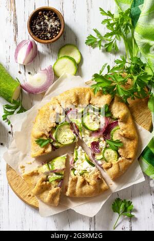 Gesunde Roggenmehl Backwaren, glutenfrei, Diät-Lebensmittel. Galette mit Zucchini, Zwiebeln und Feta-Käse auf einem Holztisch. Draufsicht flach lay Hintergrund. Stockfoto