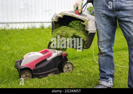 Mann mit Rasenmäher im Garten. Mann mit Rasenmäher Grassammler in der Hand. Gärtner trimmen einen Garten. Stockfoto