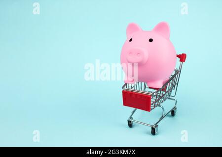 Online Business Shopping Konzept. Pink Sparschwein im Mini-Supermarkt-Trolley auf blauem Hintergrund mit Kopierplatz. Das Konzept der Einsparung von Geld auf s Stockfoto