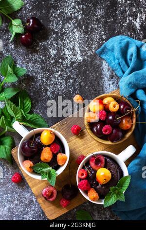 Sommerfrühstück oder Dessert. Schokoladen-Cupcake in einem Becher wird mit frischen Sommerbeeren und Kirschen serviert. Draufsicht flach lay Hintergrund. Kopieren Stockfoto