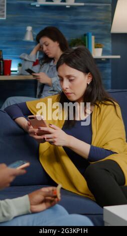 Multirassische Freunde entspannen sich auf der Couch, während sie Nachrichten im Internet surfen und dabei mobile Zeit miteinander während einer Überraschungsparty verbringen. Eine Gruppe von multiethnischen Menschen, die sich im Wohnzimmer einen lustigen Online-Film ansehen Stockfoto