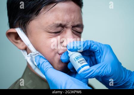 Kopfschuss eines Kindes mit medizinischer Gesichtsmaske, das eine intranasale Coronvirus-Covid-19-Impfung durch Nasenloch vom Arzt erhält - Konzept der Covid-Nasen Stockfoto