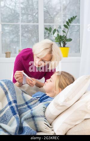 Verärgerte Mutter, die die Temperatur ihrer kleinen kranken Tochter überprüft. Stockfoto