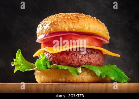 Nahaufnahme von Burger. Klassischer amerikanischer Hamburger mit Rinderfleisch, grünem Salat, Cheddar-Käse, roten Tomaten und lila Zwiebeln, mit Sesambrot Stockfoto