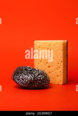 Küchenreinigungsgeräte, Spülschwamm und Metallbürste auf roter Hintergrundisolierung. Stockfoto