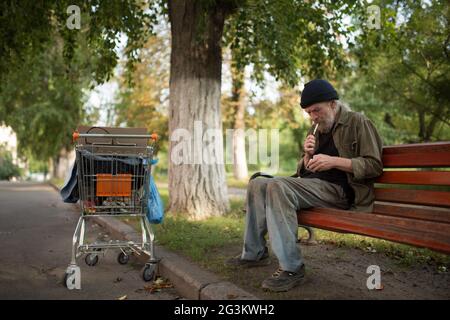 Obdachloser sitzt auf der Bank Blitz Zigarette. Stockfoto