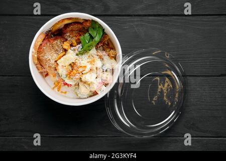 Gebratener Schinken mit Salat, bestreut mit Speckchips und geriebenem Parmesan im Take-Away-Paket Stockfoto