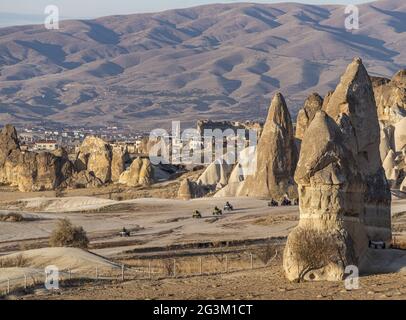 Touristen, die auf dem ATV mit der Landschaft von Feenkaminen und Weinbergen in Kappadokien, Türkei, reiten Stockfoto