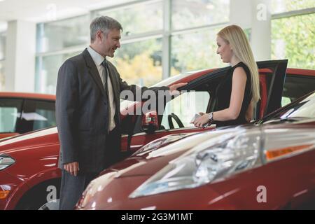 Autosalon, junge Frau, die ein Auto wählt und mit dem Händler spricht. Stockfoto