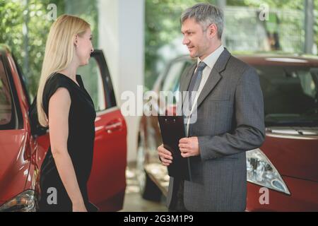 Fahrzeughändler, der Elektroauto an eine junge hübsche Frau verkauft. Stockfoto
