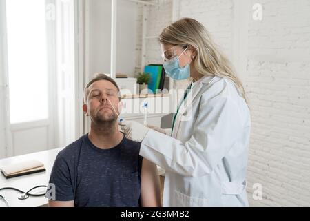 Krankenschwester testet jungen erwachsenen Mann auf Coronavirus-Infektion mit einem schnellen COVID-19-Test. Arzt, der einen nasalen Tupfer am Mann durchführt, der eine Probe nimmt, um zu analysieren, ob p Stockfoto