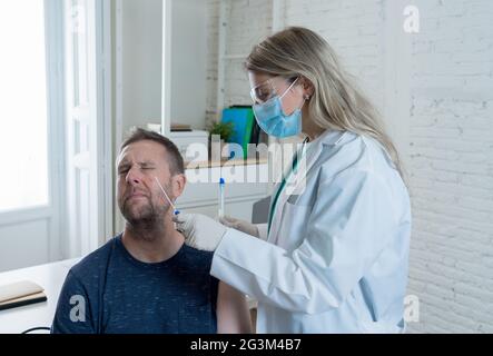 Krankenschwester testet jungen erwachsenen Mann auf Coronavirus-Infektion mit einem schnellen COVID-19-Test. Arzt Durchführung Nasenabstrich auf verängstigten Mann unter Probe zu Analy Stockfoto