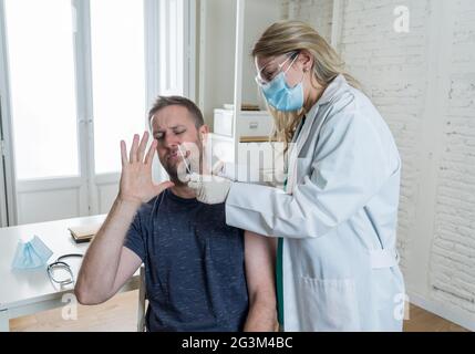 Krankenschwester testet jungen erwachsenen Mann auf Coronavirus-Infektion mit einem schnellen COVID-19-Test. Arzt Durchführung Nasenabstrich auf verängstigten Mann unter Probe zu Analy Stockfoto