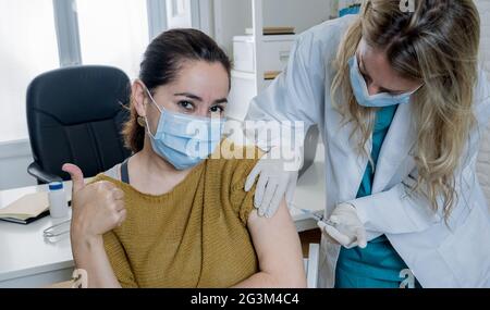 Ärztin oder Krankenschwester, die junge Frau in der Klinik impft. Männlicher Patient, der gegen Coronavirus geimpft wird, erhält einen Covid-Impfstoff intramuskulär in Stockfoto