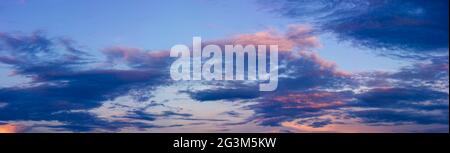 Panorama von blauem Himmel, Sonnenuntergang und dunklen dramatischen Wolken, die von der orangen Sonne beleuchtet werden. Stockfoto