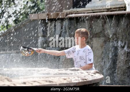 Der Junge spielt mit den Wasserstrahlen des Springbrunnens Four Seasons auf dem Manezhnaya-Platz. Kind genießt den Sommer, heißes Wetter Stockfoto