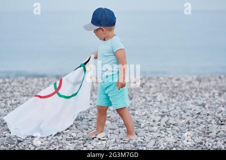 Kemer, Türkei - 16. Juni 2021: Kleiner Junge mit olympischer Flagge an der Küste. Konzept der Olympischen Spiele. Das Konzept der Hoffnung und des Glaubens an Erfolg. Stockfoto