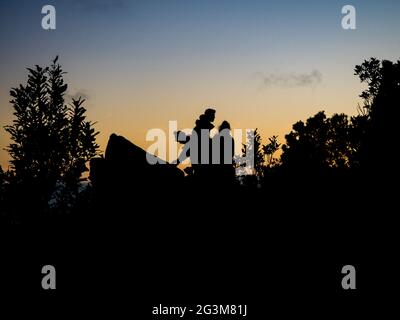 Silhouetten von begeisterten Wanderern sitzen auf einem Felsen, um den Sonnenaufgang zu beobachten Stockfoto