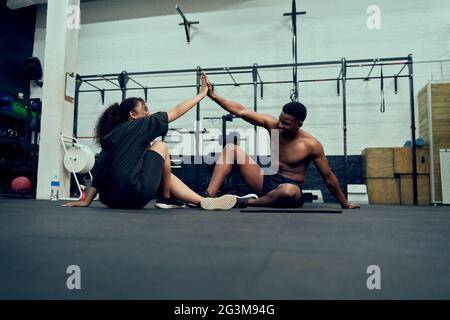 Mixed-Race-Freunde, die im Fitnessstudio Cross-Fit machen. Männlicher Personal Trainer, der afroamerikanischen Frauen nach dem Training einen High-Five gab. Hochwertige Fotos Stockfoto