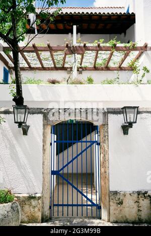 Steinzaun mit Gittertoren in der Nähe des Hauses mit Balkon, Baum und Grün Stockfoto