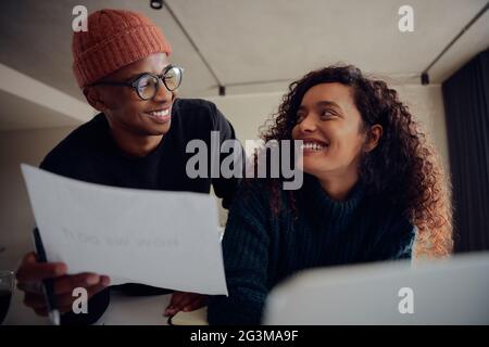 Nahaufnahme eines gemischten Rennpaares mit Laptop für Online-Banking. Glückliches afroamerikanisches Paar, das lächelt und einander anschaut, während es zusammenarbeitet Stockfoto
