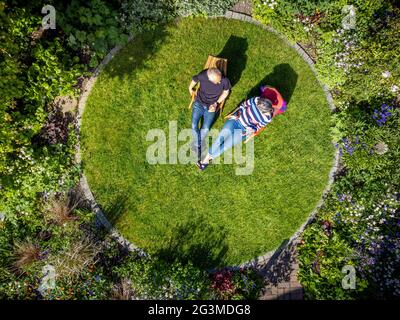 Luftaufnahme des Hausgartens mit kreisförmigem Rasen und reifen, lässig gekleideten kaukasischen Männern und Frauen saßen auf hölzernen Liegestühlen. Stockfoto