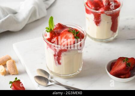 Italienische Tiramisu mit Erdbeeren. Mehrlagiges Dessert in Gläsern mit Cookie Savoyardi, Mascarpone und Schlagsahne auf weißem Hintergrund. Nahaufnahme. S Stockfoto