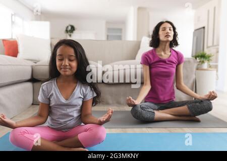 Lächelnde hispanische Mutter und Tochter meditieren im Wohnzimmer Stockfoto