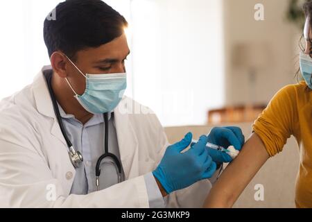 Hispanischer Arzt, der weiblichen Patienten zu Hause eine Covid-Impfung mit Gesichtsmasken verabreicht Stockfoto