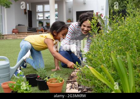 Lächelnde hispanische Mutter und Tochter im Garten, knien und Pflanzen in Blumenbeet Stockfoto