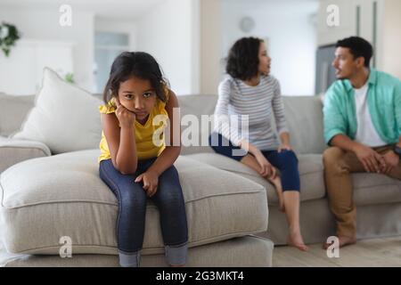 Traurige hispanische Tochter, die auf der Couch sitzt und Mutter und Vater hinter sich streiten Stockfoto