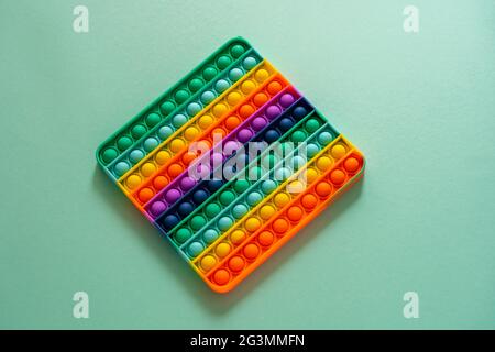 Helles Silikon gestreiftes Spielzeug Big Pop IT Nahaufnahme auf blauem Hintergrund. POPIT für Kinder, die mit Regenbogen spielen, die Blasen mit den Fingern drücken, oben Stockfoto