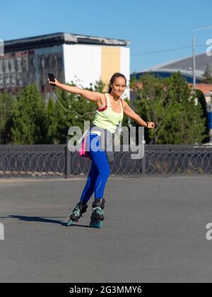 Porträt einer jungen Frau beim Rollerblading. Sie hört Musik über Kopfhörer von ihrem Smartphone und genießt das Leben. Stockfoto