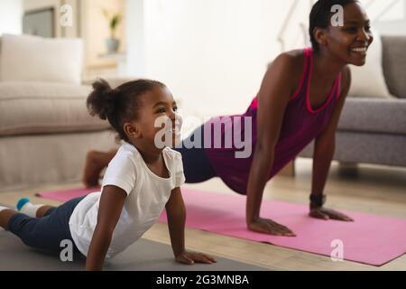 Lächelnde afroamerikanische Mutter und Tochter praktizieren Yoga und liegen auf gestreckten Matten Stockfoto