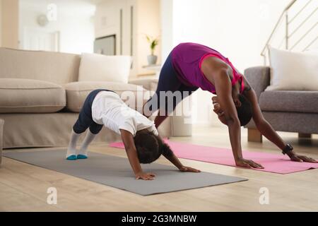 Lächelnde afroamerikanische Mutter und Tochter praktizieren Yoga und strecken sich auf Matten im Wohnzimmer Stockfoto