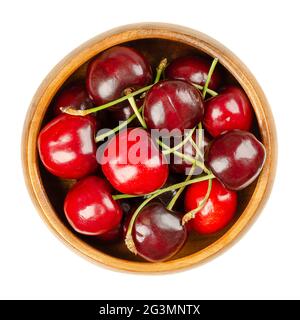 Fresh cherries, in a wooden bowl, ready to eat. Red and ripe fruits of the true cherry species Prunus avium, a stone fruit cultivar. Close-up. Stockfoto