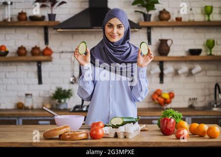 Hübsche muslimische Frau, die beim Kochen Zucchinischeiben zeigt Stockfoto