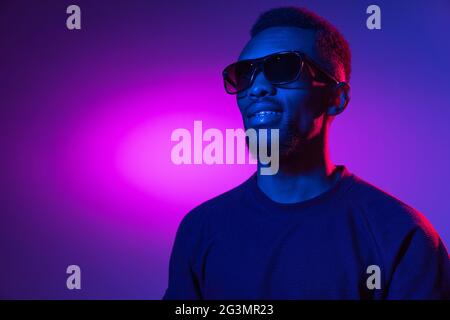 afroamerikanischer junger Mann auf dunklem Studiohintergrund in Neon. Konzept der menschlichen Emotionen, Gesichtsausdruck, Jugend, Verkauf, Werbung. Stockfoto