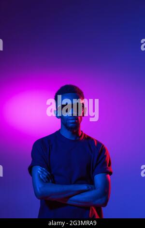 afroamerikanischer junger Mann auf dunklem Studiohintergrund in Neon. Konzept der menschlichen Emotionen, Gesichtsausdruck, Jugend, Verkauf, Werbung. Stockfoto