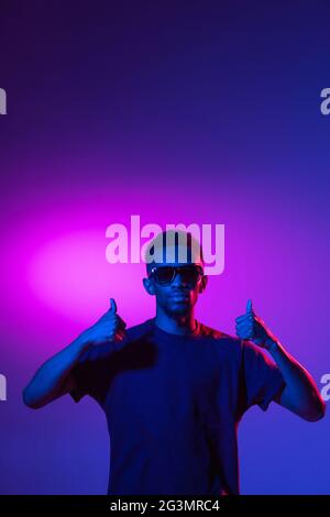 afroamerikanischer junger Mann auf dunklem Studiohintergrund in Neon. Konzept der menschlichen Emotionen, Gesichtsausdruck, Jugend, Verkauf, Werbung. Stockfoto