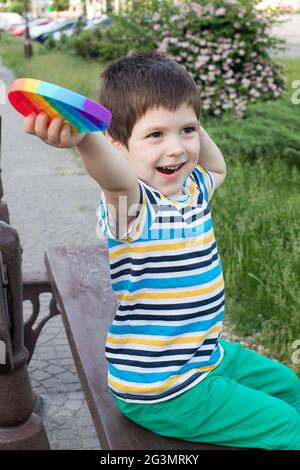 Ein kleiner Junge spielt mit Pop IT im Stadtpark. Antistress-Spielzeug für die Entwicklung von Feinmotorik bei Kindern. Vertikales Foto. Stockfoto