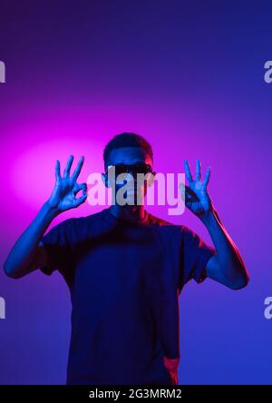 afroamerikanischer junger Mann auf dunklem Studiohintergrund in Neon. Konzept der menschlichen Emotionen, Gesichtsausdruck, Jugend, Verkauf, Werbung. Stockfoto