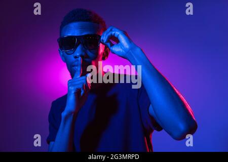 Afrikanischer junger Mann auf dunklem Studiohintergrund in Neon. Konzept der menschlichen Emotionen, Gesichtsausdruck. Stockfoto