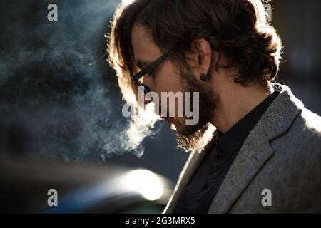 Ein Mann mit langen Haaren raucht außerhalb Stockfoto