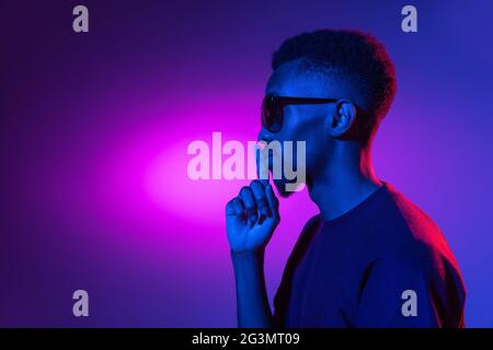 Afrikanischer junger Mann auf dunklem Studiohintergrund in Neon. Konzept der menschlichen Emotionen, Gesichtsausdruck. Stockfoto